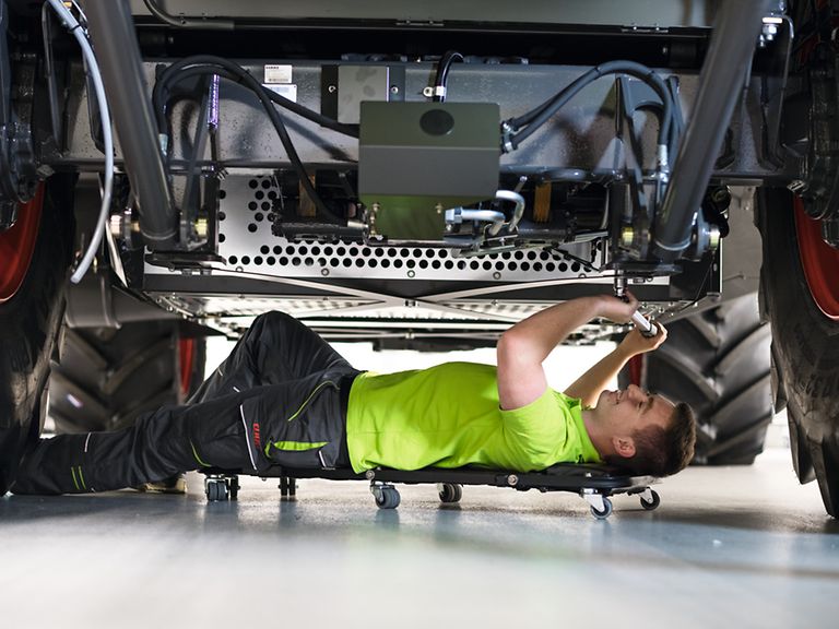 specialist-for-metal-technology- Auszubildender liegt unter Mähdrescher und schraubt.