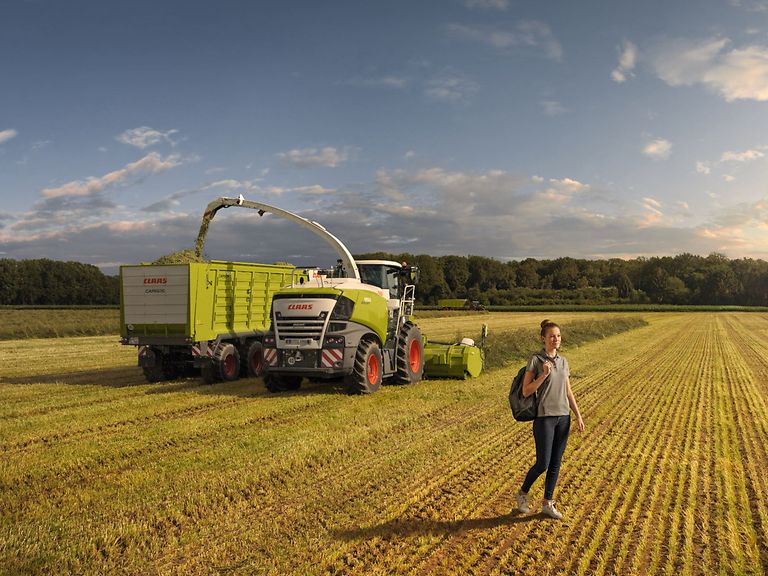 pupil-internship Person mit Rucksack vor einem Feldhäcksler.