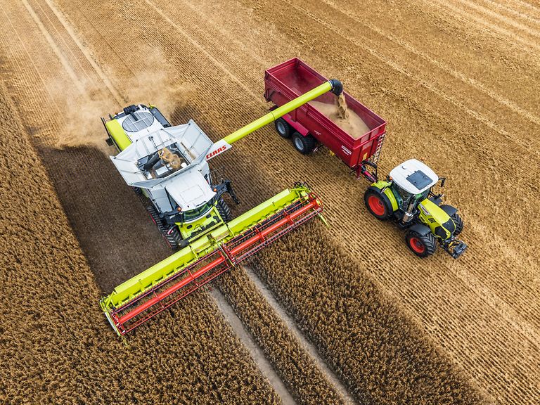 469563_27 LEXION 6900 с CONVIO FLEX 1080 во время уборки овса, рядом с ним трактор и прицеп-погрузчик.