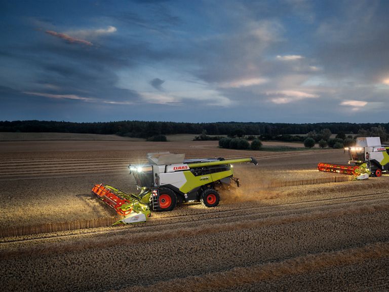 460034_27 LEXION 6900 із CONVIO 1080 під час збирання пшениці ввечері з увімкненим робочим освітленням.